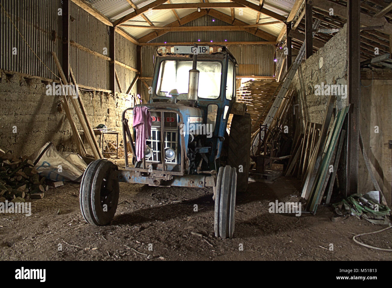 An old ford tractor being renovated in an old barn with the morning sun streaming through the cab. Stock Photo