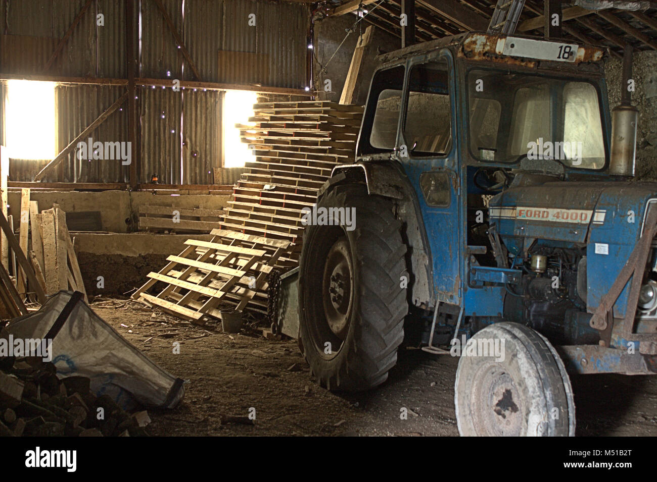 Ford Tractor being refurbished in a barn. Its early morning and the barn has sunlight streaming in through the windows. Stock Photo