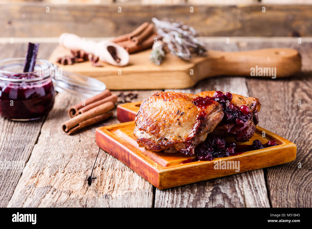 Roast chicken legs on cutting board served with cranberry sauce on rustic wooden table Stock Photo