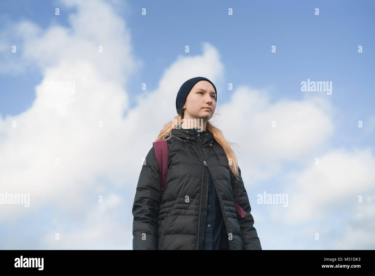 low angle shot of teen girl outdoors on a cold day agains sky with clouds, epic shot Stock Photo