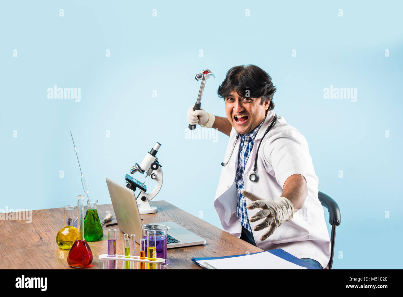 Asian/Indian male scientist or doctor or science student experimenting with microscope and chemicals, laptop and smartphone in a lab Stock Photo
