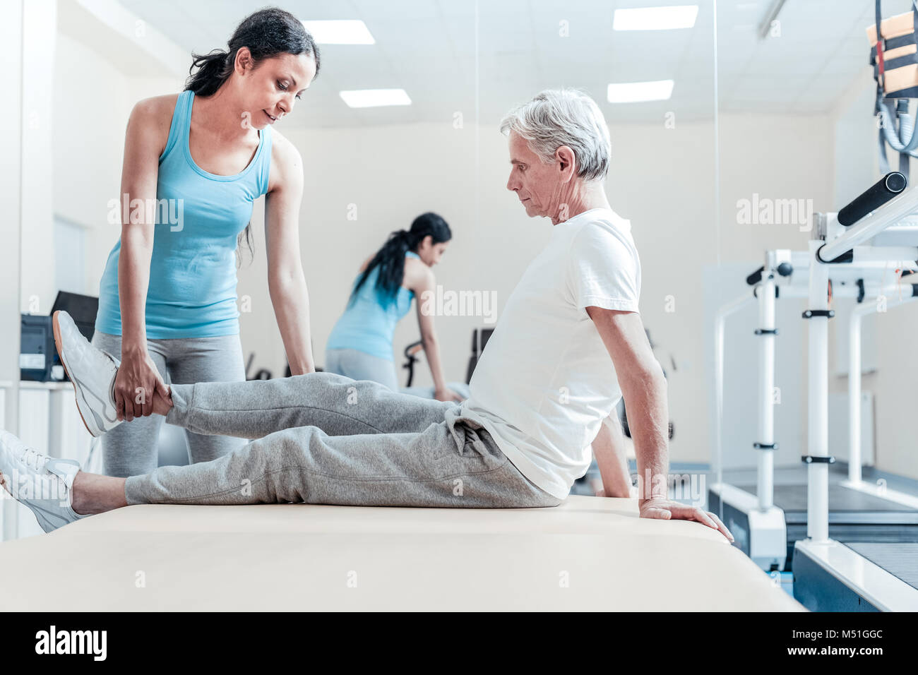 Serious trainer raising old crippled mans leg Stock Photo Alamy