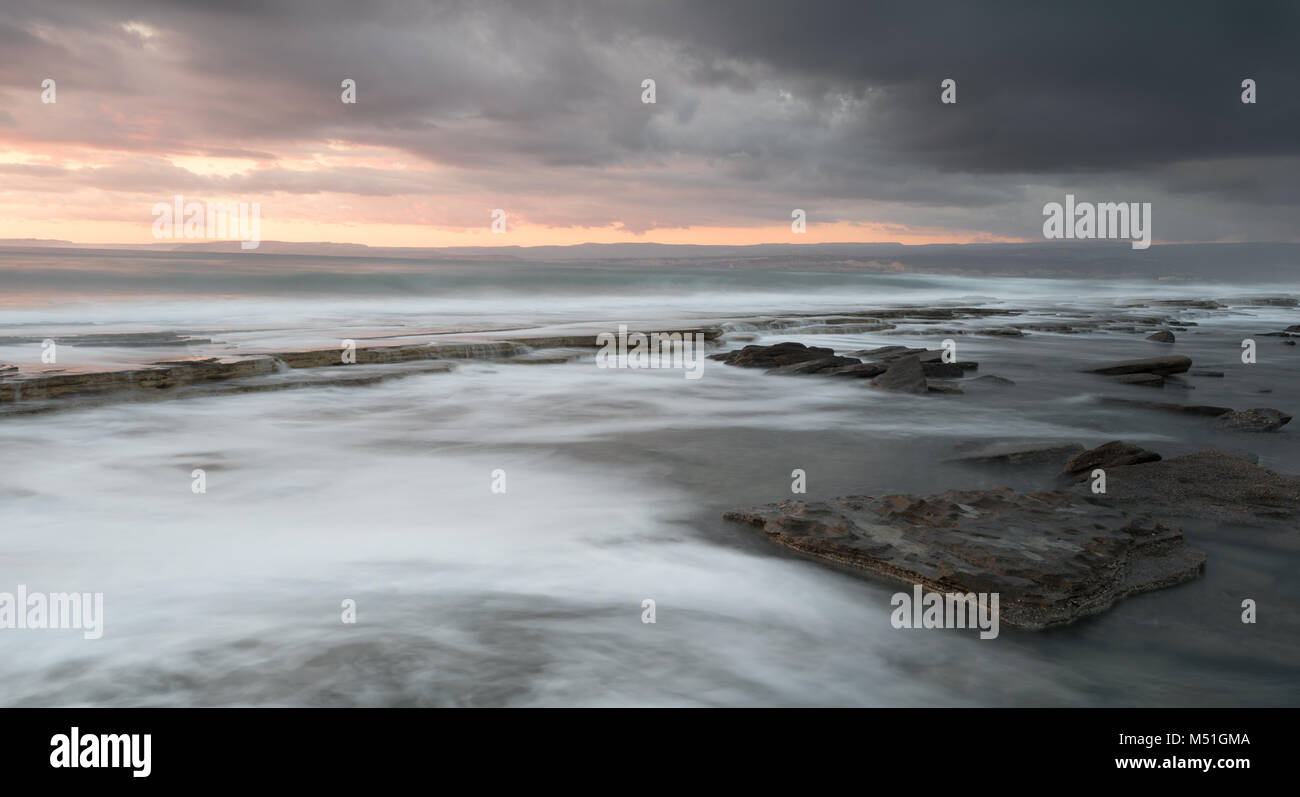 Rocky seashore seascape with wavy ocean and waves crashing on the rocks during a dramatic and beautiful sunset at Akrotiri coast area in Limassol, Cyp Stock Photo