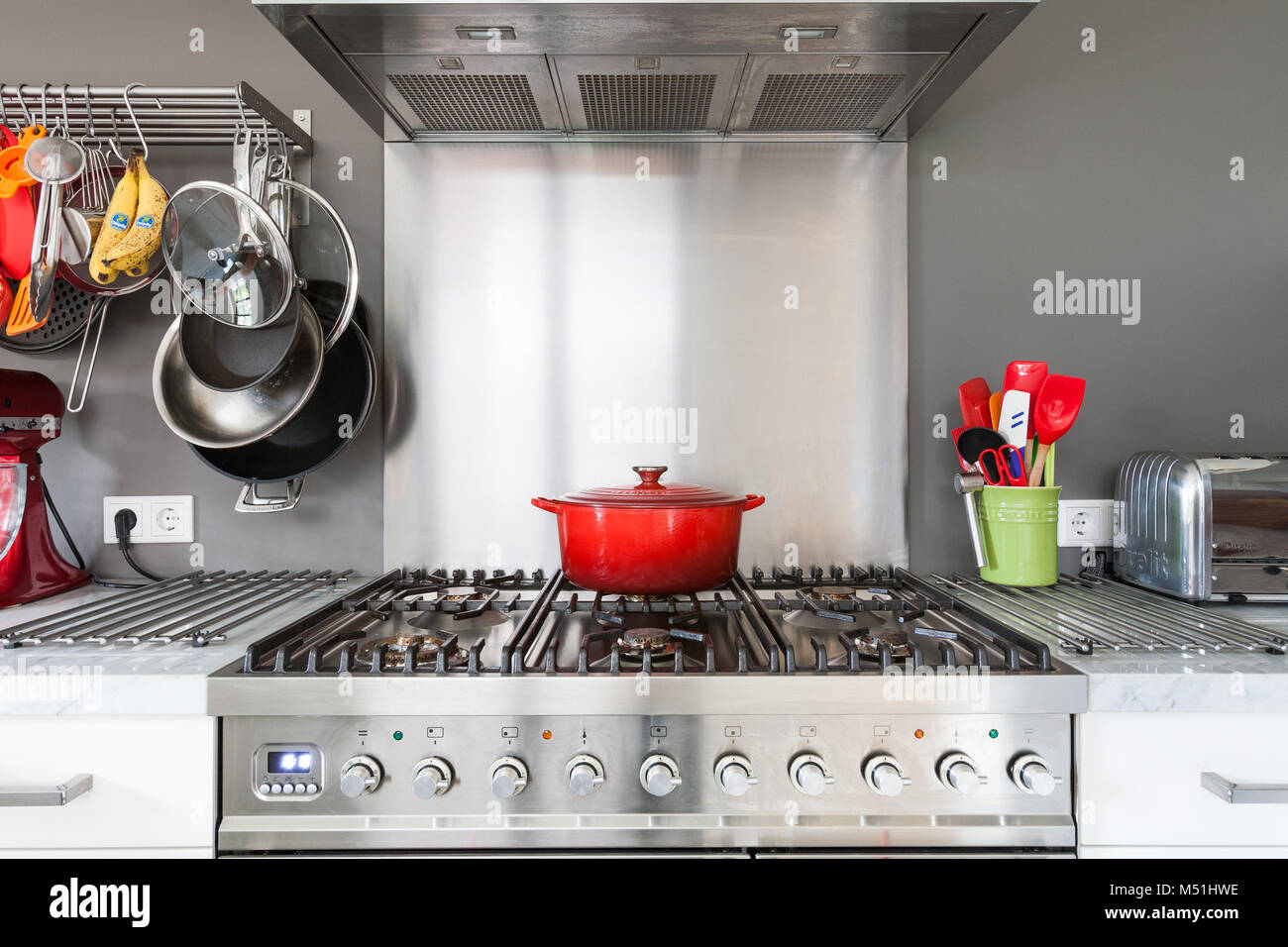 A bright red casserole dish sits atop a high end, stainless steel stove Stock Photo