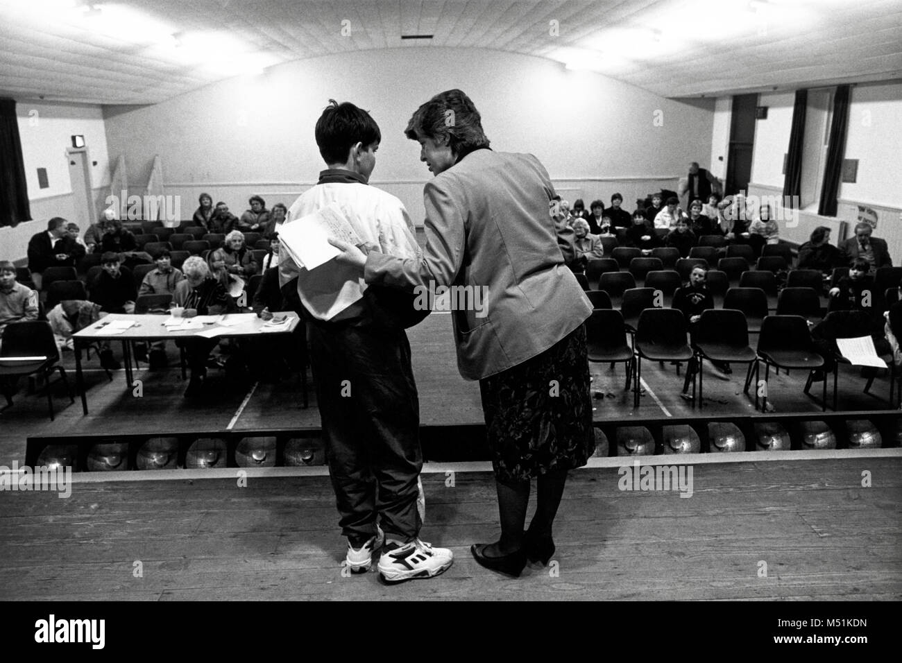Boy waiting to perform being spoken to by female announcer on stage at small eisteddfod in village hall Trawsfynydd Gwynedd North Wales UK Stock Photo