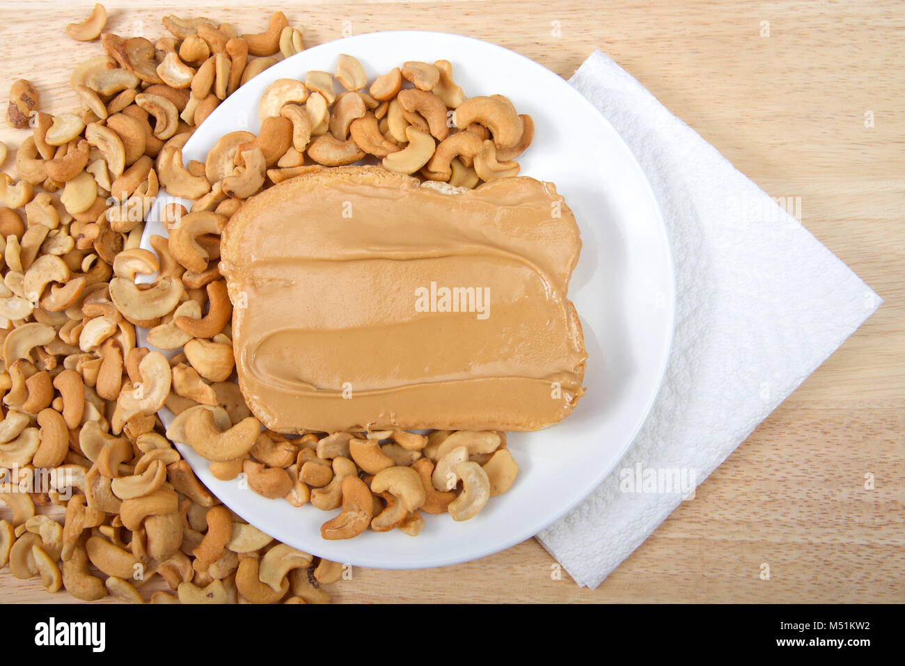 Cashew butter spread on bread on a white plate surrounded by cashew nuts. Cashews are a good source of plant protein, contain no cholesterol and are l Stock Photo