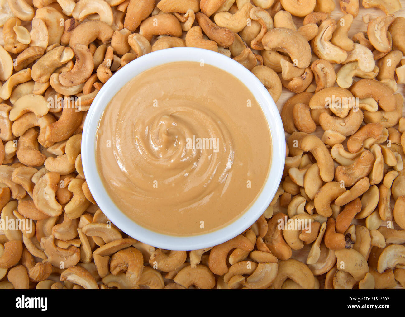 White bowl with fresh cashew butter surrounded by cashew nuts. Cashews
