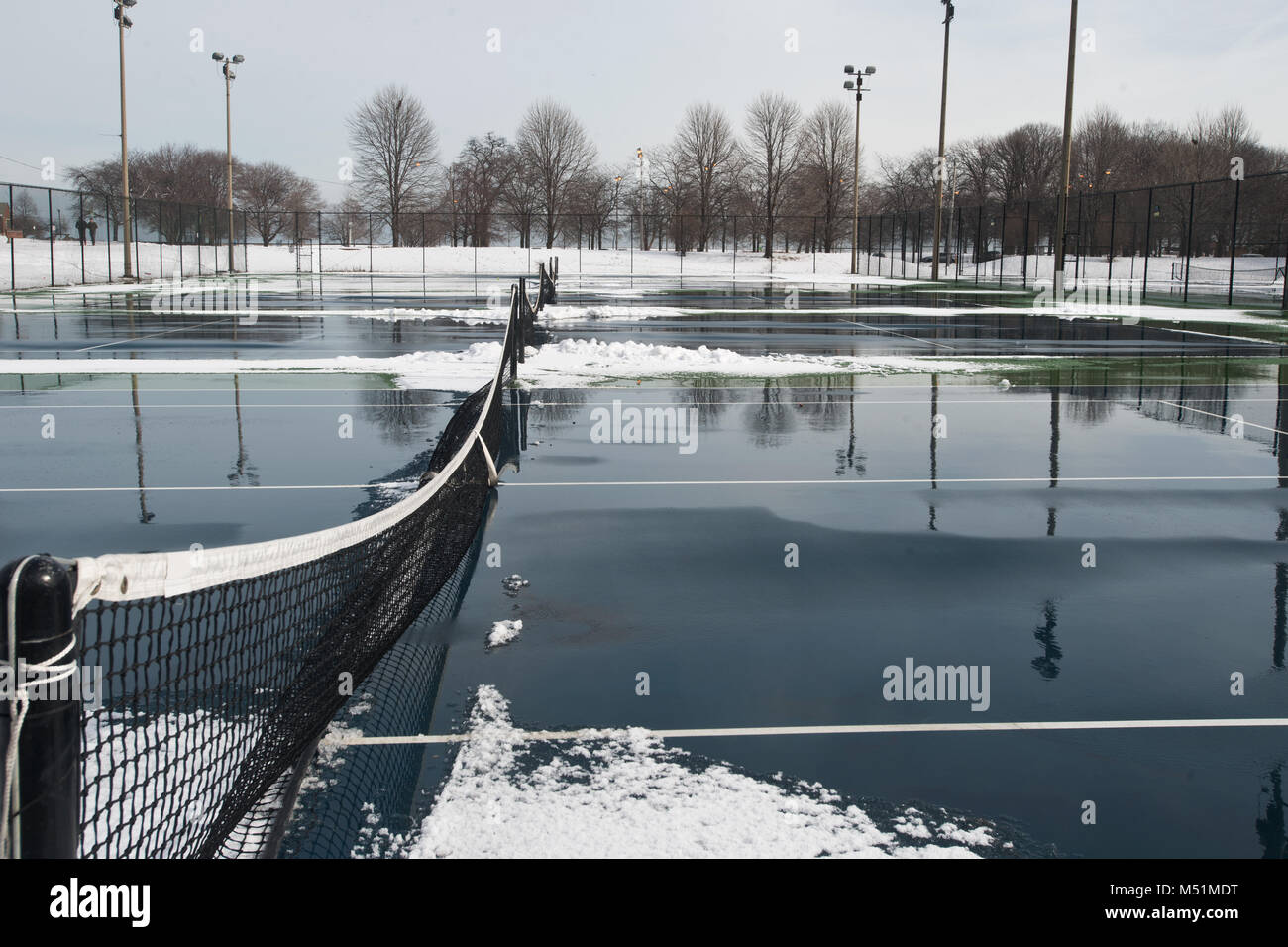 Public hard tennis court covered with snow and water waiting for spring