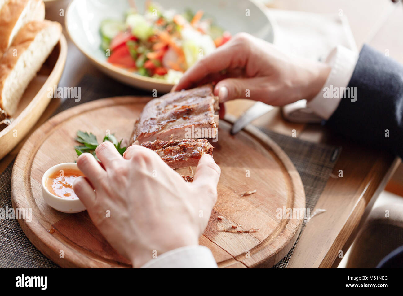 the man in the restaurant with a knife cuts grilled pork ribs. Serving