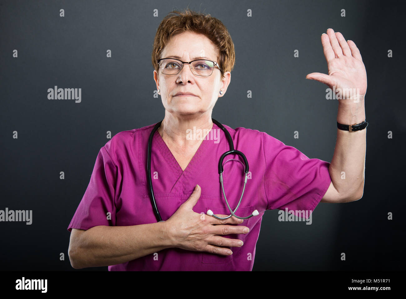 Portrait of senior lady doctor taking oath on black background Stock
