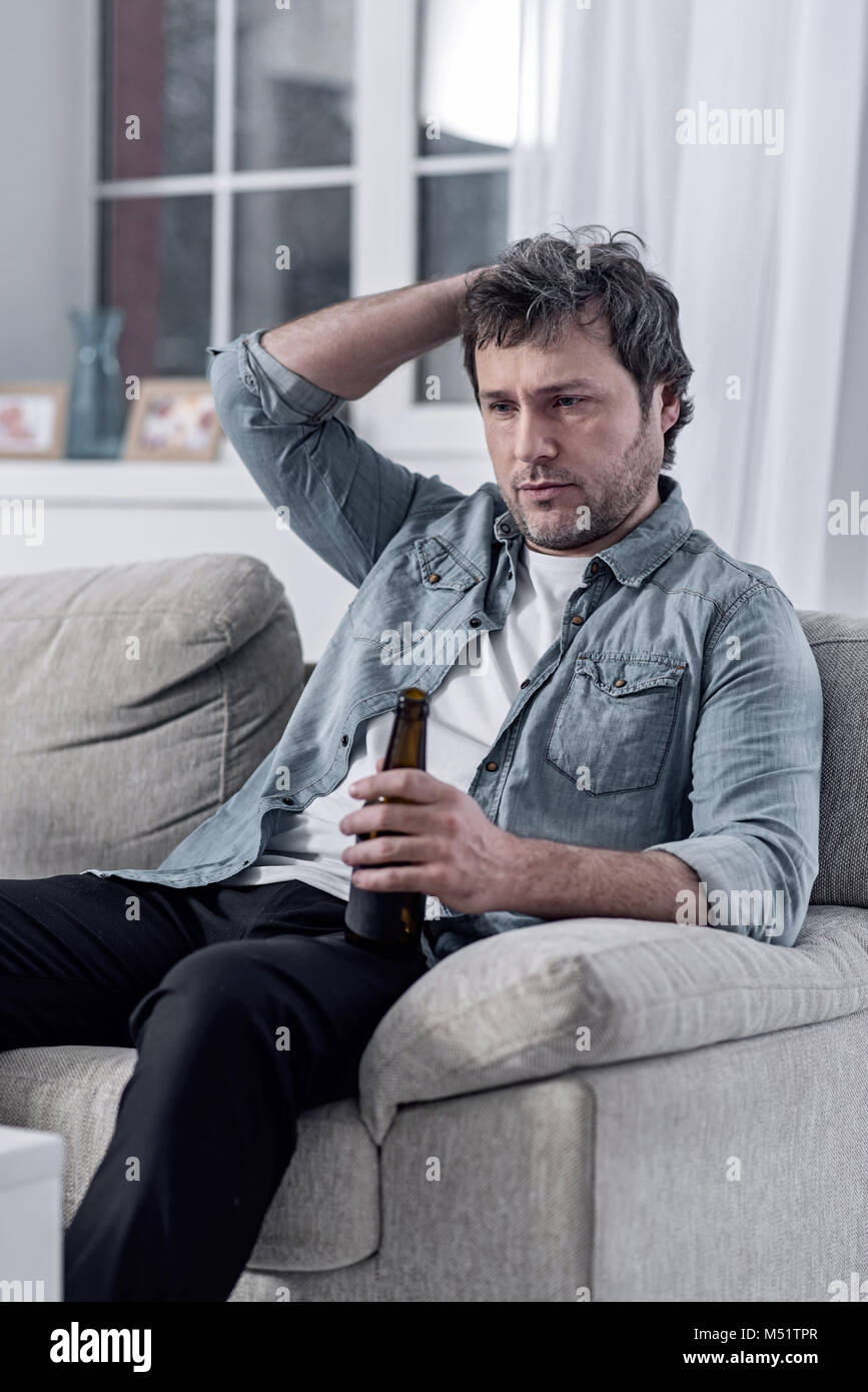 Depressed man scratching his head while drinking alcohol alone Stock Photo