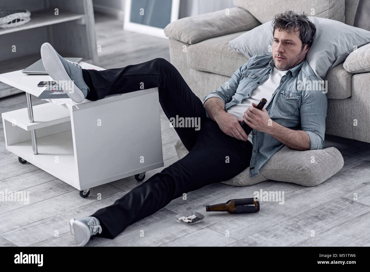 Unshaved man relaxing with his leg on a table and drinking alcohol Stock Photo