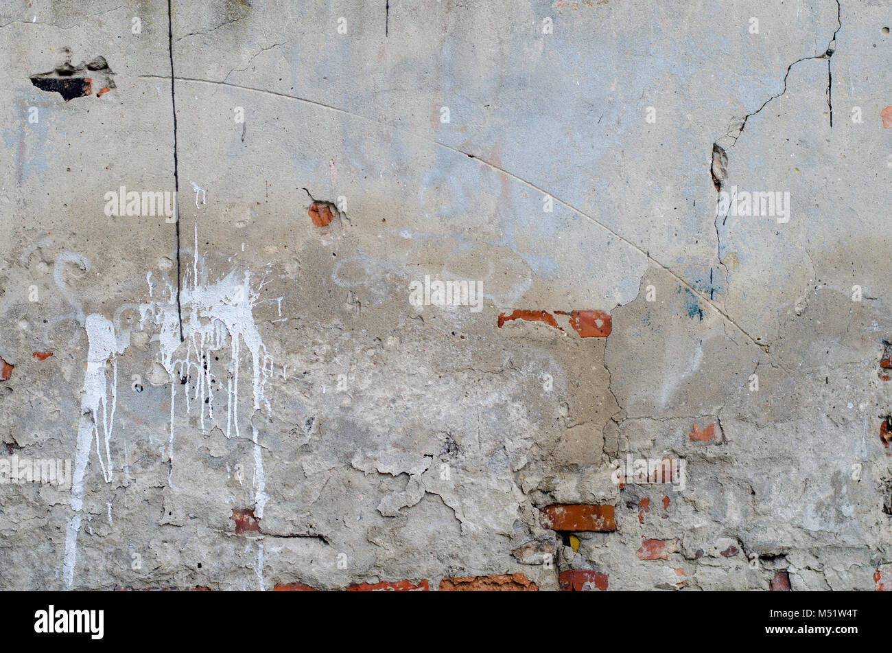 old grey concrete garage wall with red bricks, cracks and white spots
