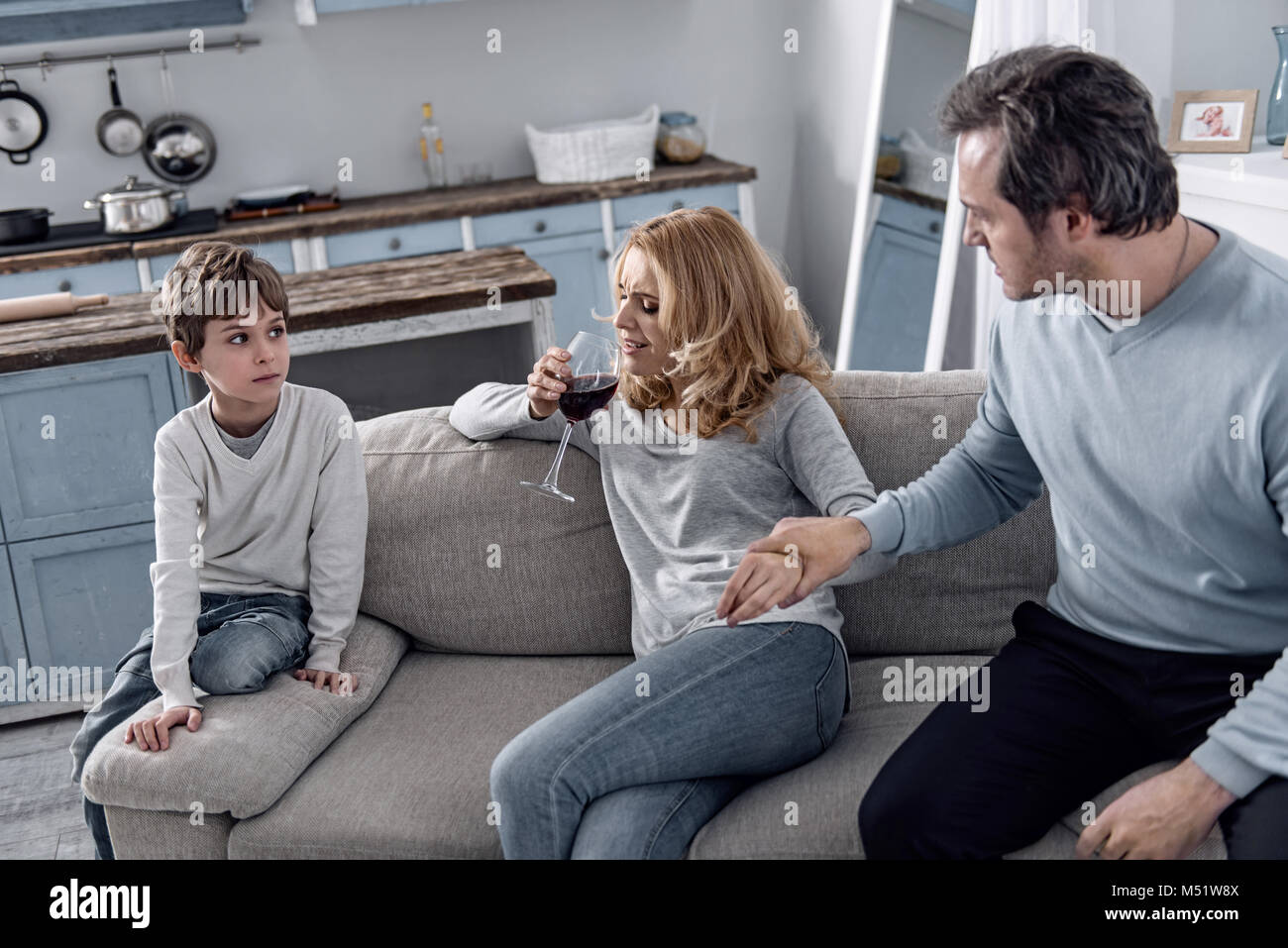 Emotional woman drinking wine and her husband preventing it Stock Photo