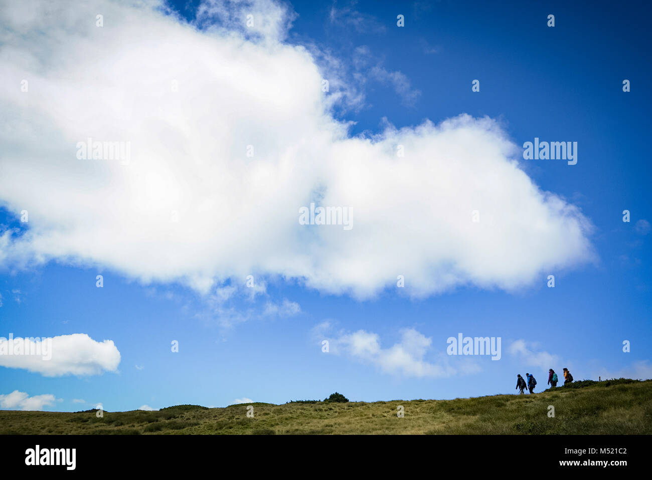 Big cloud in sunny sky over a group of people hiking in french alps Stock Photo