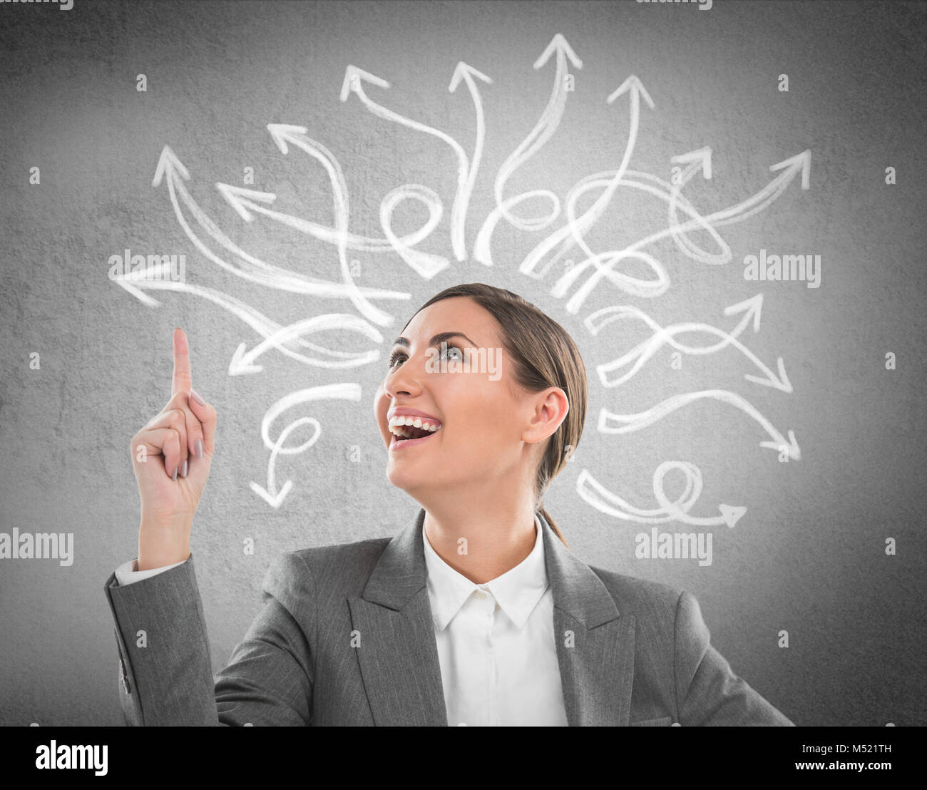 Happy, young businesswoman looking at many twisted arrows on the concrete wall overhead Stock Photo