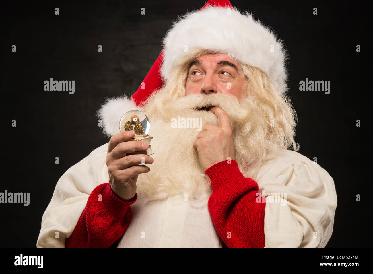Santa Claus holding snow globe against dark background Stock Photo - Alamy