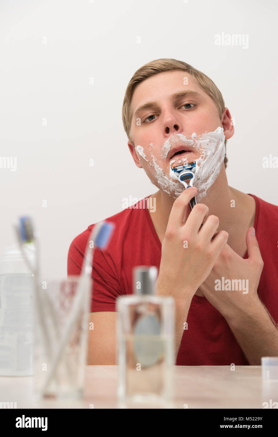 Young man shaving in the bath. He is passing the razor for the beard