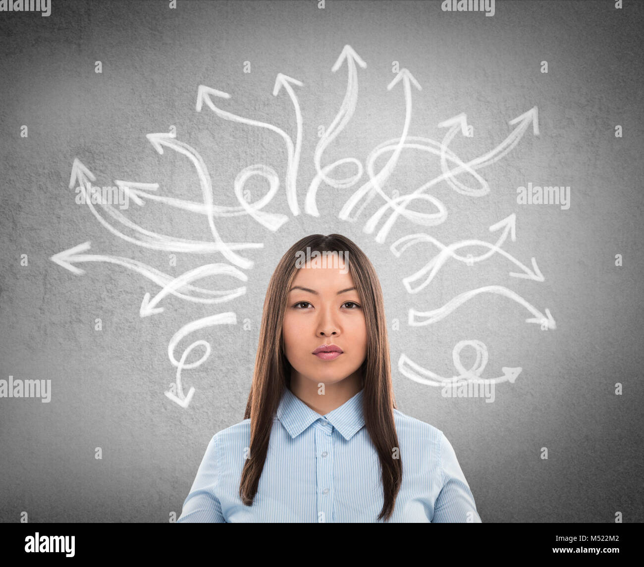 Serious, young businesswoman with many twisted arrows on the concrete wall overhead Stock Photo