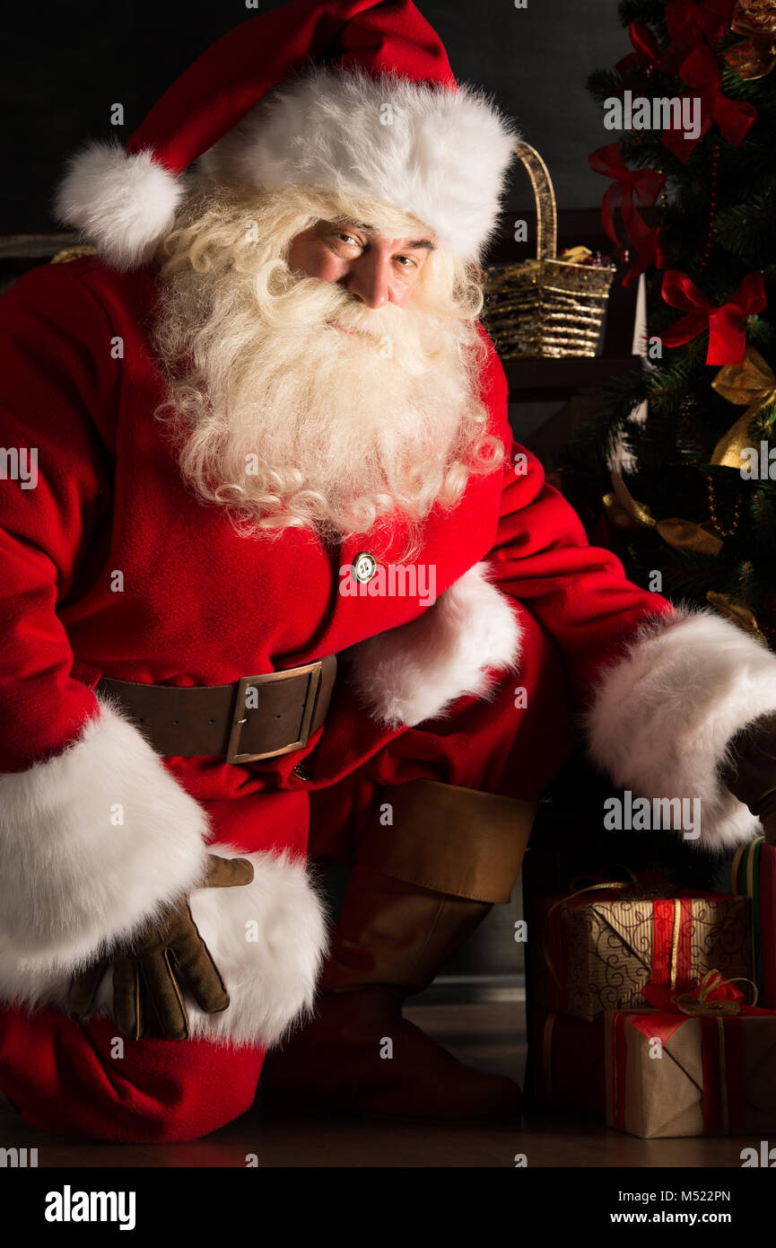 Santa placing gifts under Christmas tree in dark room Stock Photo - Alamy