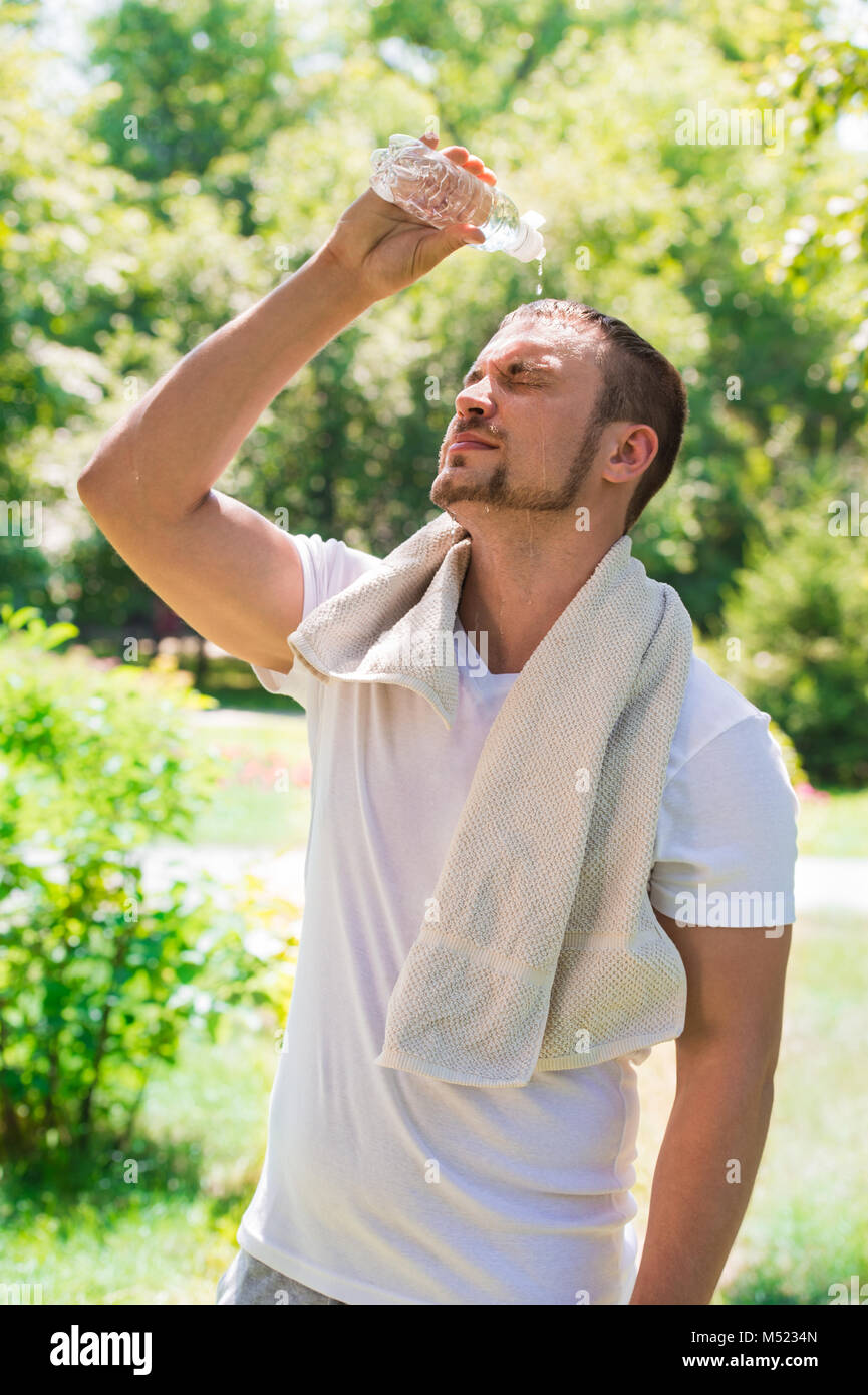 Sport fitness man. Young athletic man cooling himself after training by squirting water over himself from a drinks bottle outdoors at park Stock Photo