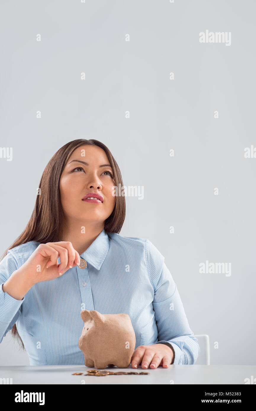 Young happy business woman putting money in the piggybank and dreaming