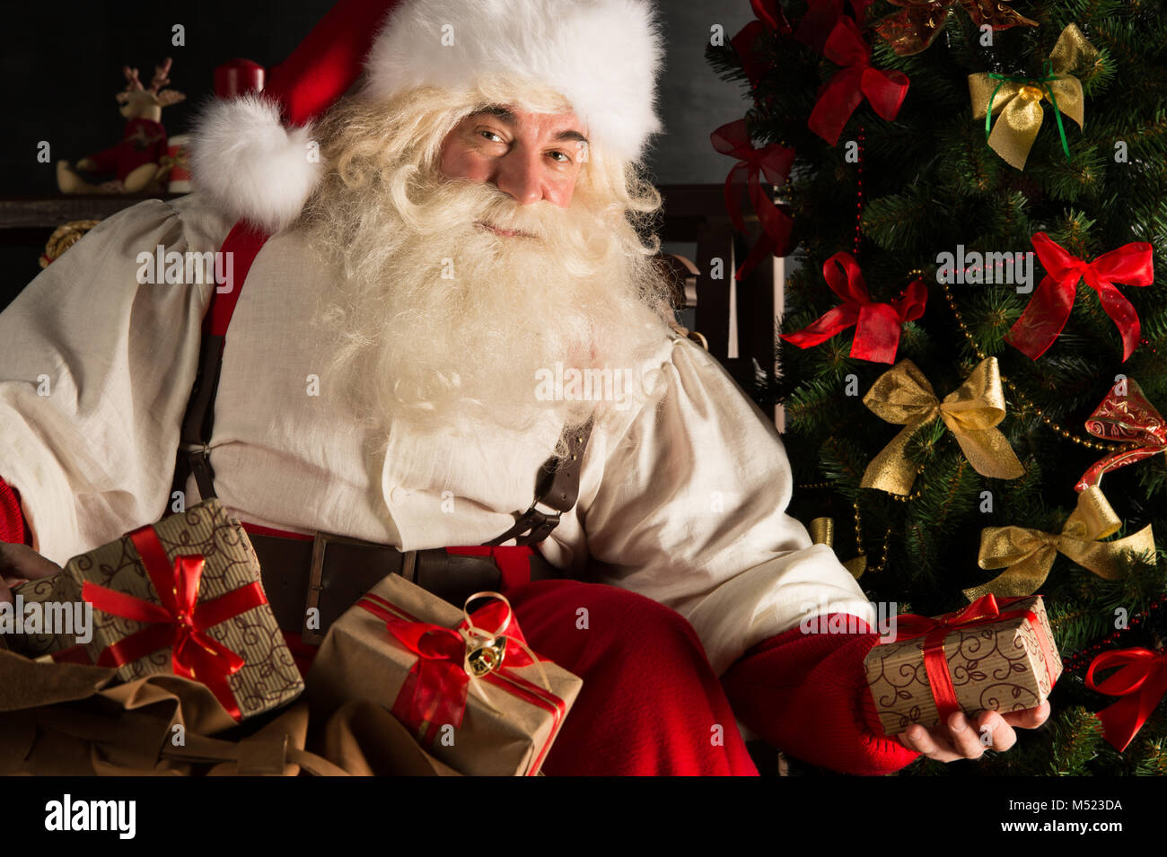 Santa putting gifts under Christmas tree in dark room Stock Photo - Alamy
