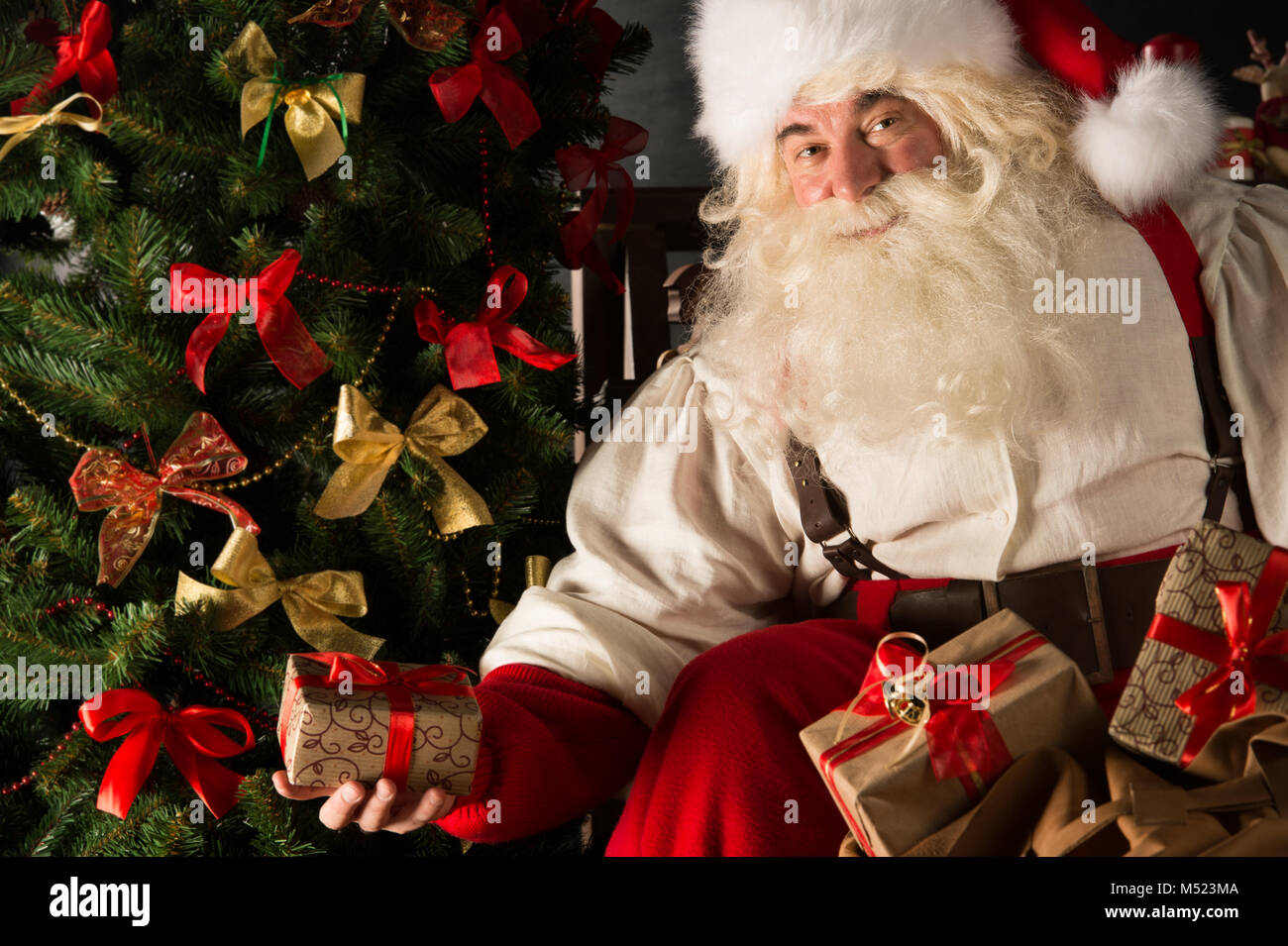 Santa placing gifts under Christmas tree in dark room Stock Photo - Alamy