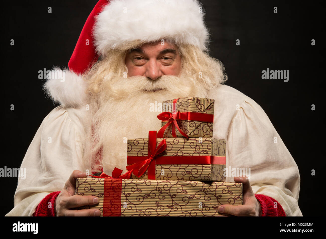 Santa Claus carrying big stack of Christmas gifts against dark ...