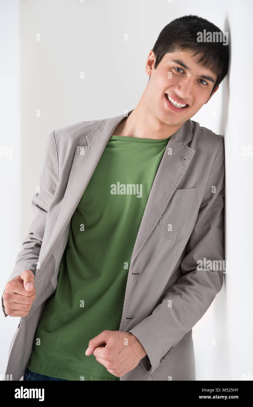Happy smiling young man leaning against white wall Stock Photo - Alamy