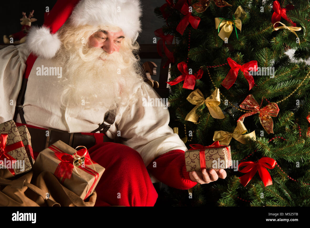 Santa putting gifts under Christmas tree in dark room Stock Photo Alamy