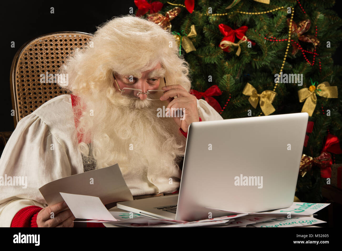 Santa Claus working on computer reading emails and paper letters from children from all over the world Stock Photo