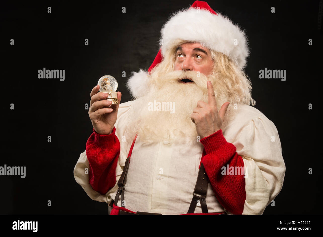 Santa Claus holding snow globe against dark background Stock Photo - Alamy