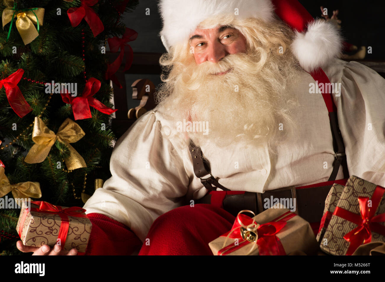 Santa putting gifts under Christmas tree in dark room Stock Photo - Alamy