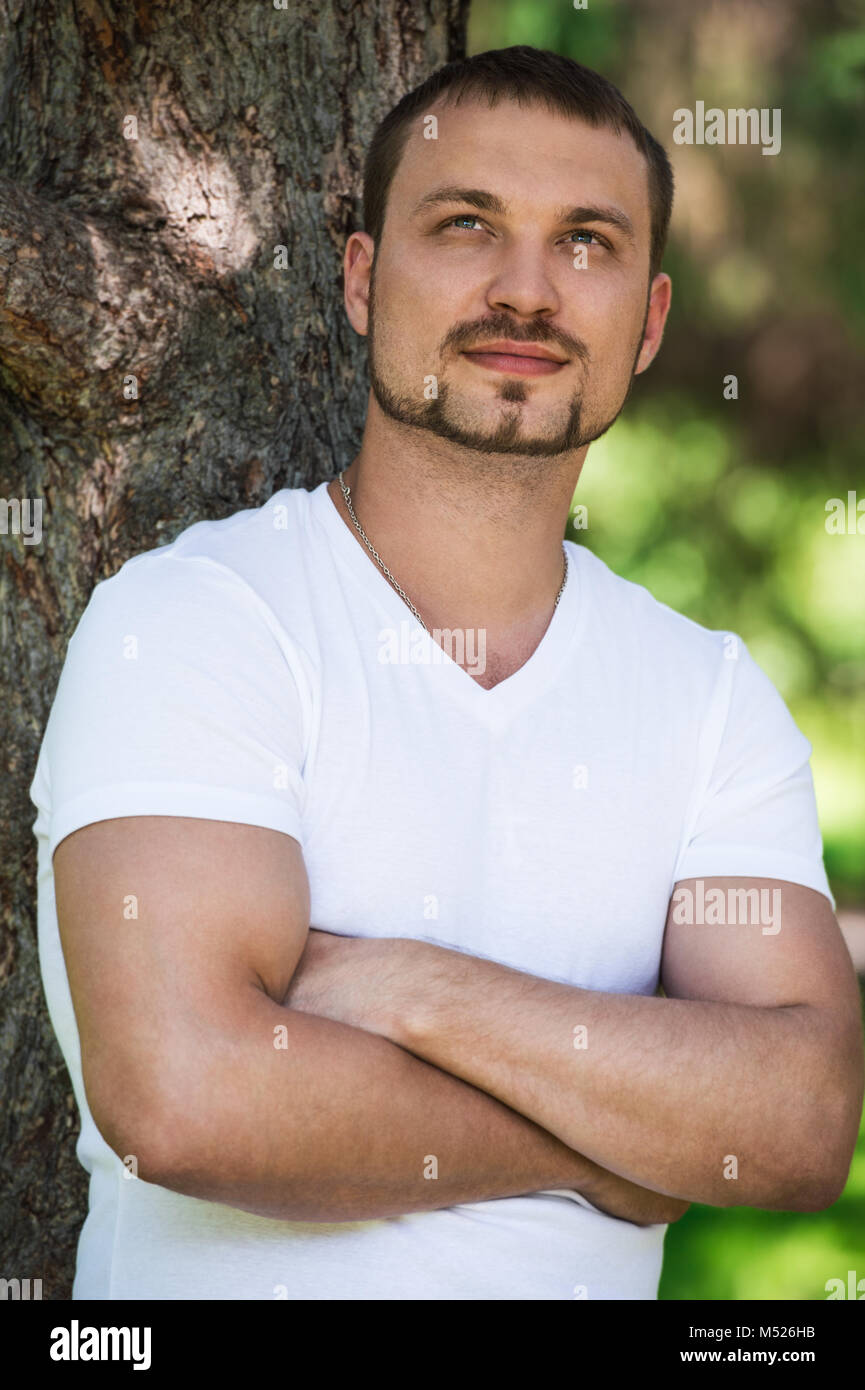Smiling handsome man outdoors dreaming and leaning on tree. He is confident in his bright future Stock Photo