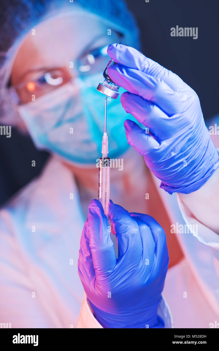 Doctor drawing up solution from vaccine bottle and filling syringe ...