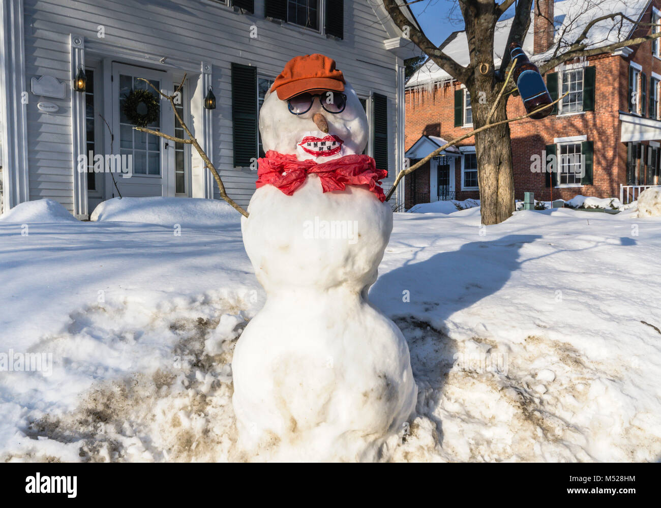 Funny snowman adorned with bucktooth smile, baseball cap, and bottle of beer. Stock Photo