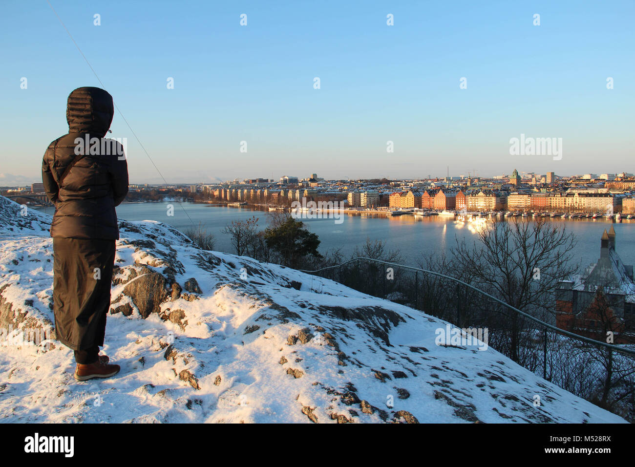 Woman viewing Kungsholmen island in central Stockholm from the top of Skinnarviksberget on a cold and sunny winter day. Stock Photo