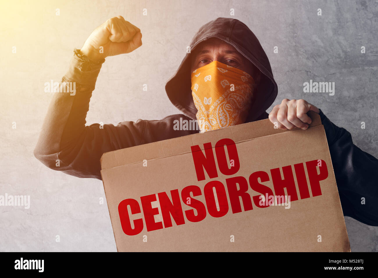 Hooded activist protestor holding No Censorship protest sign. Man with hoodie and scarf over face taking part in activism and fighting for the cause. Stock Photo