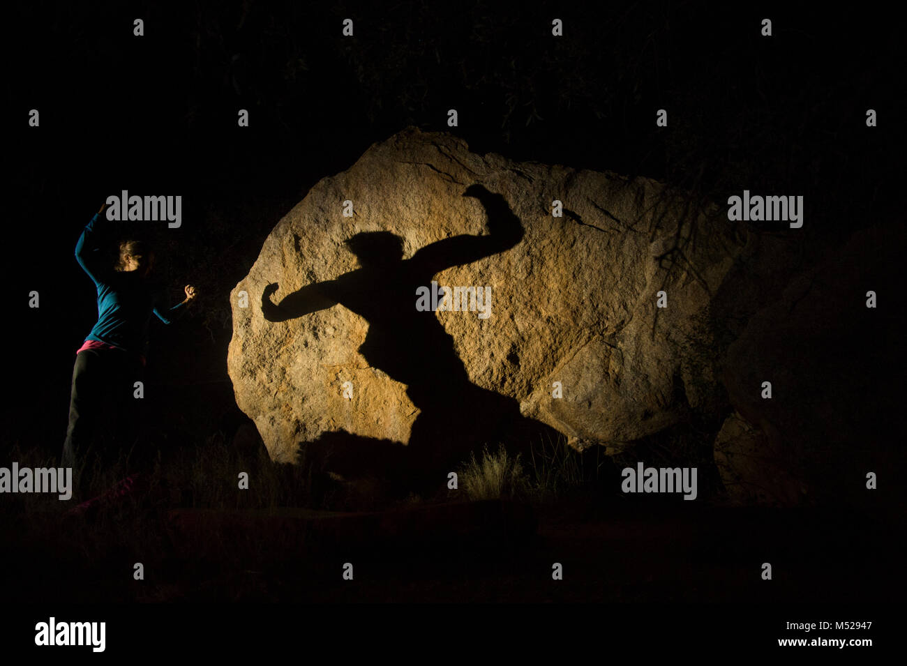 Woman flexing and casting shadow on large illuminated boulder at night