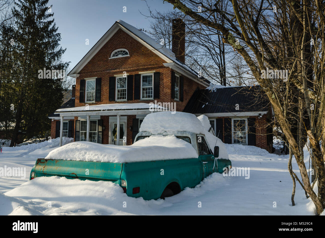Green pickup truck covered in snow in front of red brick colonial house in Grafton, VT. Stock Photo
