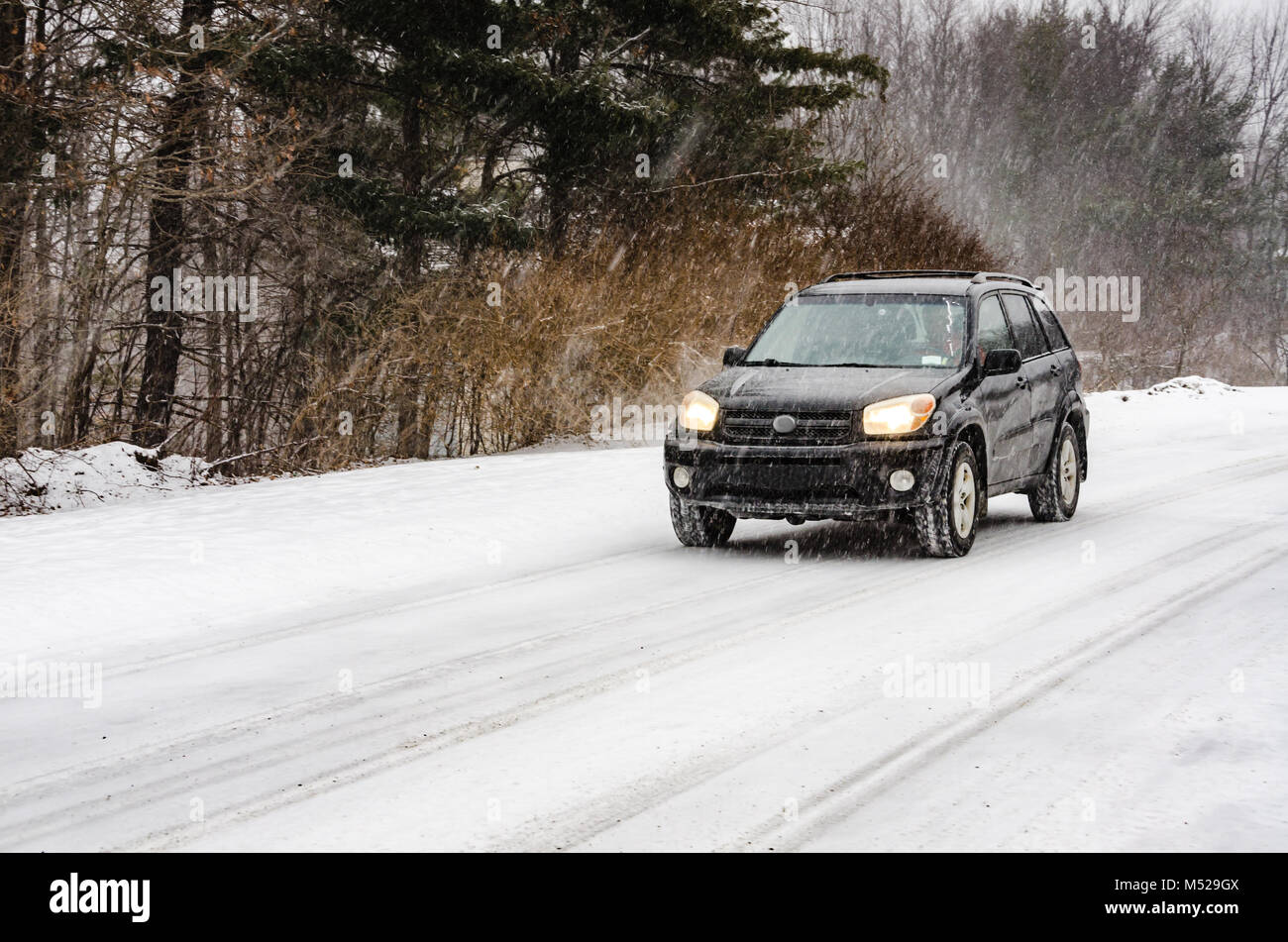 Black SUV driving on rural road in heavy snow fall. Stock Photo