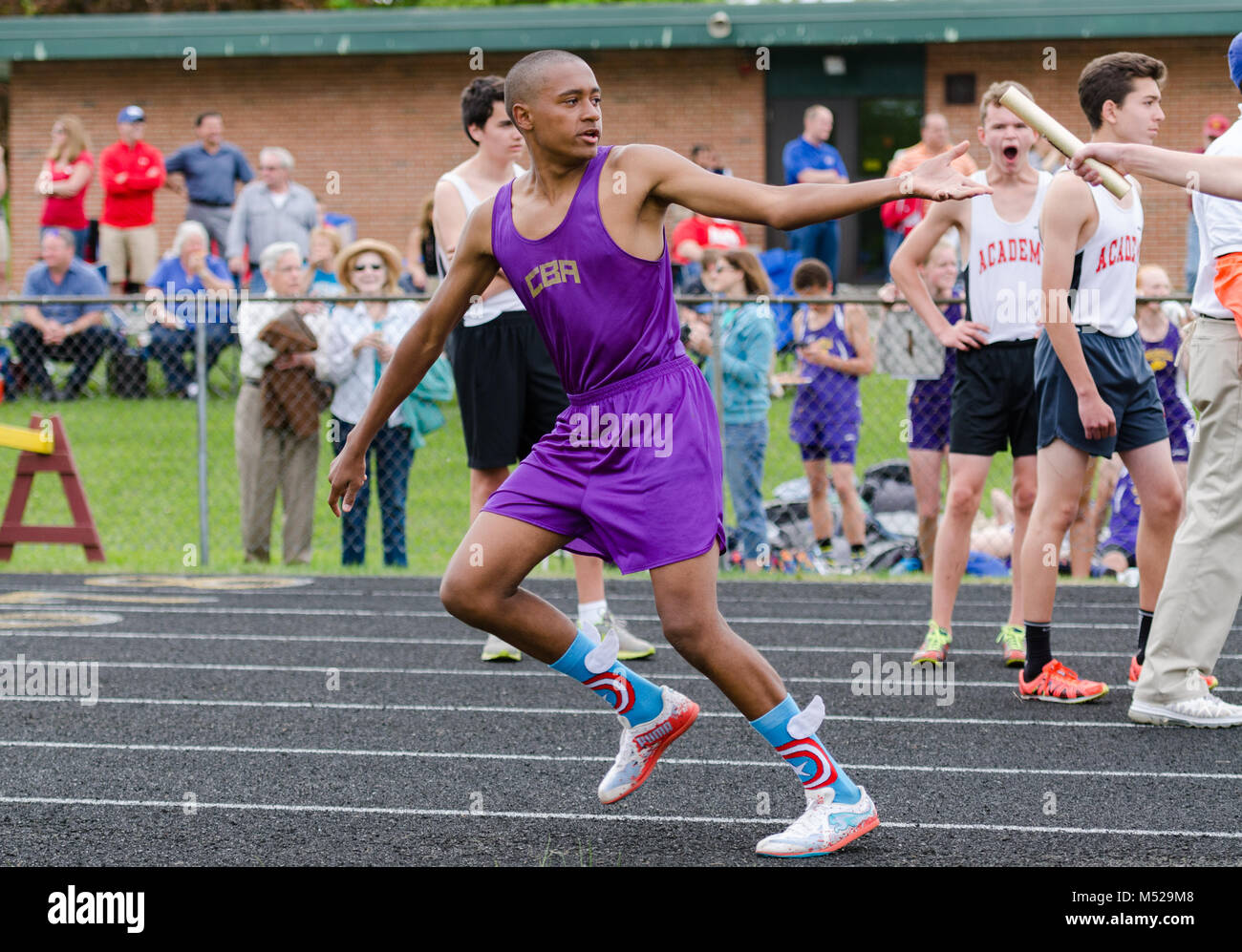 Teen boy accepts baton in relay race at outdoor track and field meet in Albany, NY on May 14, 2015. Stock Photo