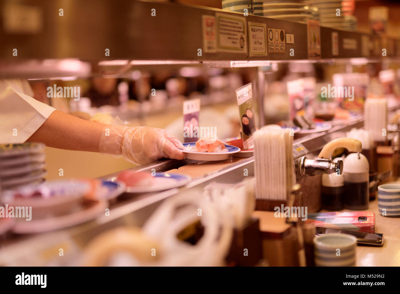 Closeup of a sushi chef's hand placing a plate of sushi on a conveyor belt at Musashi Sushi, famous conveyor-belt sushi restaurant, Kaitenzushi, in Ky Stock Photo
