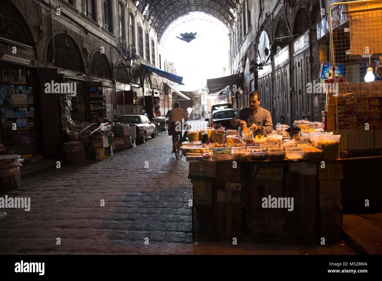 A man sells goods in Al-Hamidiyah Souq, in the old city of Damascus. Despite the ongoing conflict in Syria, life in government-held parts of Damascus still carries on relatively peacefully. Damascus, the capital city of war-torn Syria, is mostly under control by the official Syrian government led by president Bashar al-Assad. Stock Photo