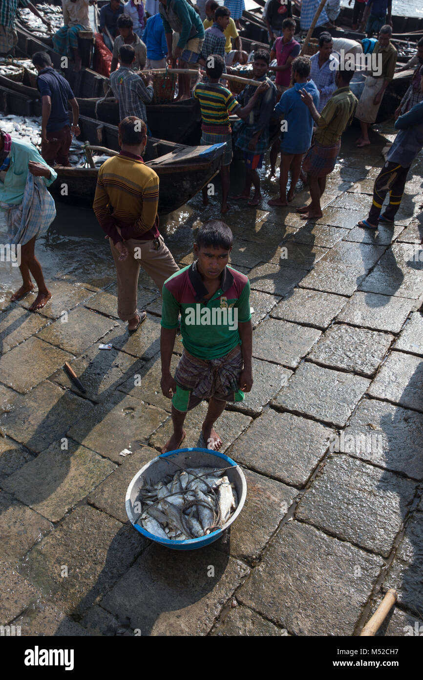 A young Bengali man stands by a container of freshly caught fish on the