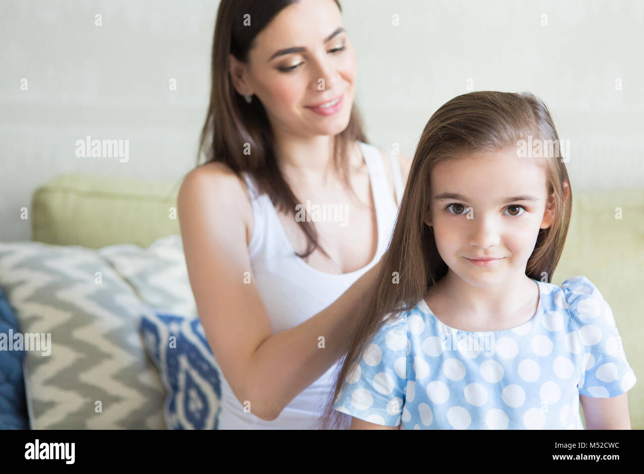 Adorable young family in living room. Mother combing her daughter's hair. Happiness and love concept Stock Photo