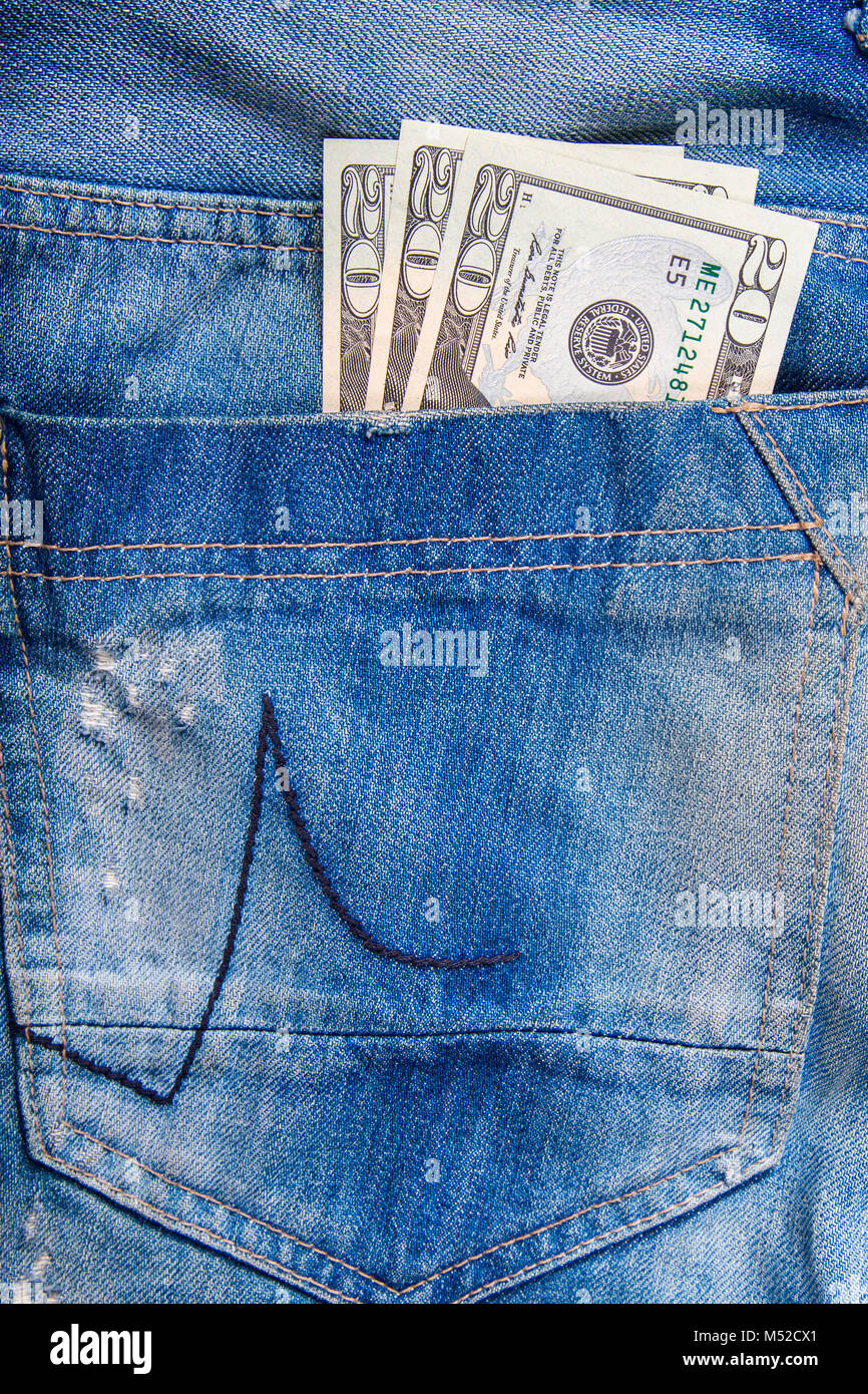 $ 20 bill in the pocket of jeans, jeans neatly stacked on wooden background, top view Stock Photo