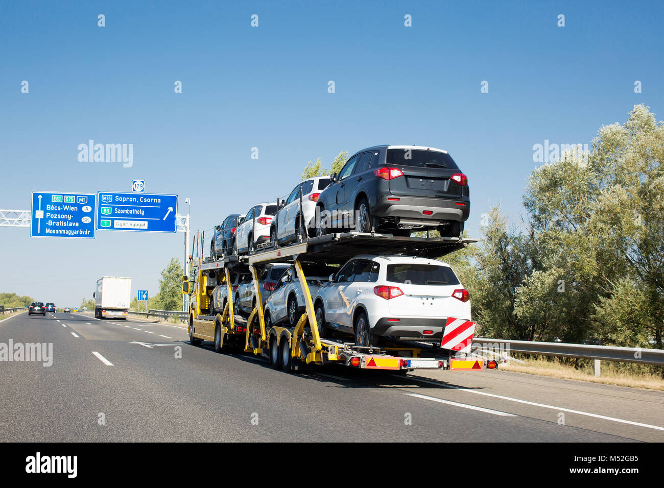 Big car carrier trailer with new cars for sale on bunk platform. Car transport truck on the highway Stock Photo