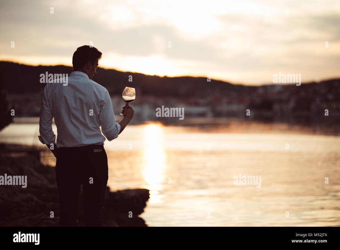 Young stressed business man drinking wine alone.Alcoholic man unhappy with his life,addicted to alcohol.Binge drinking.Alone with a drink in his hand. Stock Photo